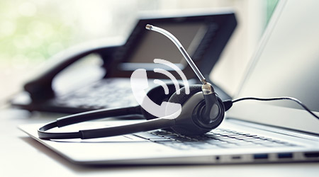 Laptop with desk phone in the background and VoIP Telecoms headset resting on keyboard.